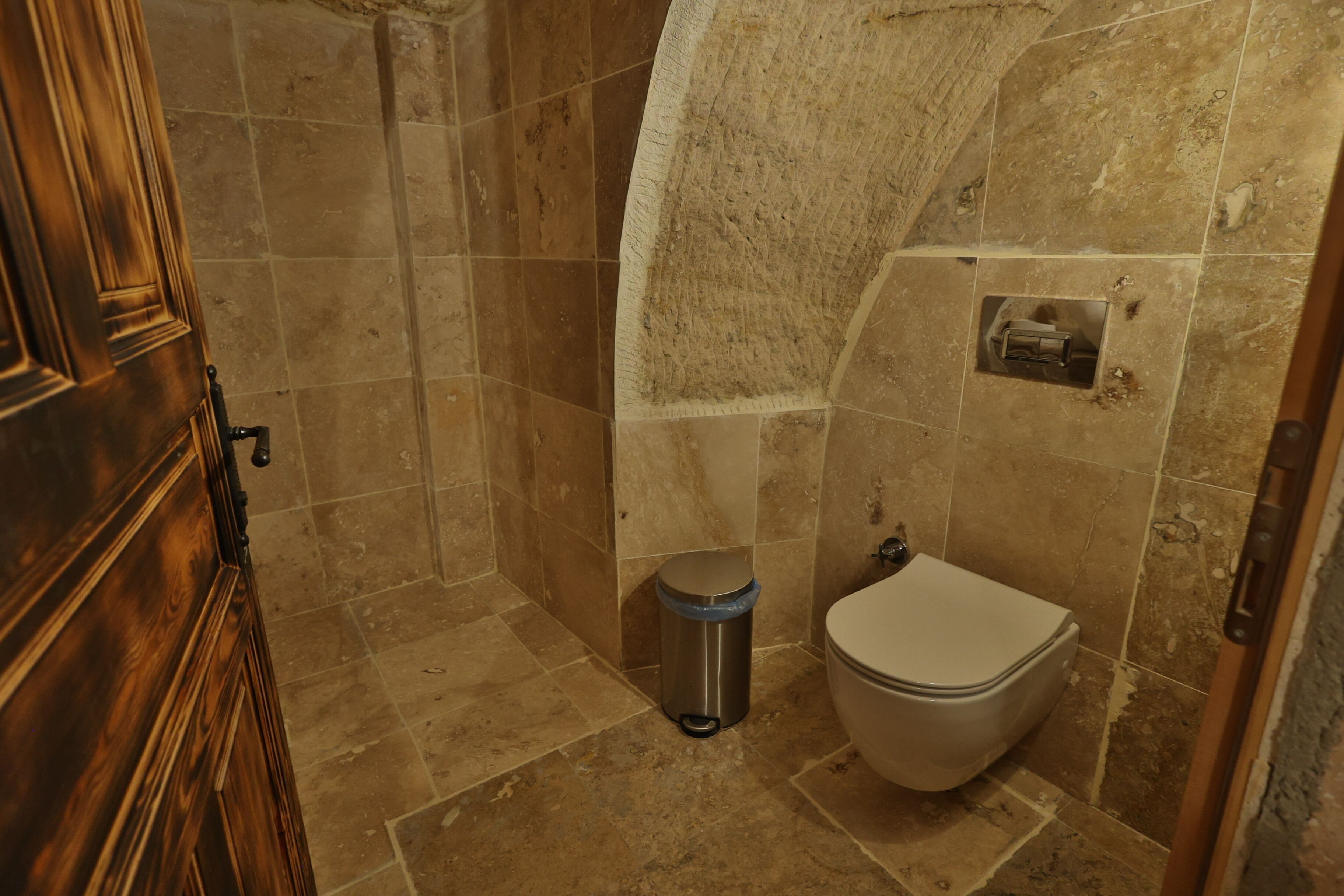 Une salle de bain avec une porte en bois, des toilettes et une poubelle.