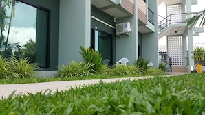 Un edificio moderno con fachada verde, mesas al aire libre y un jardín bien cuidado.