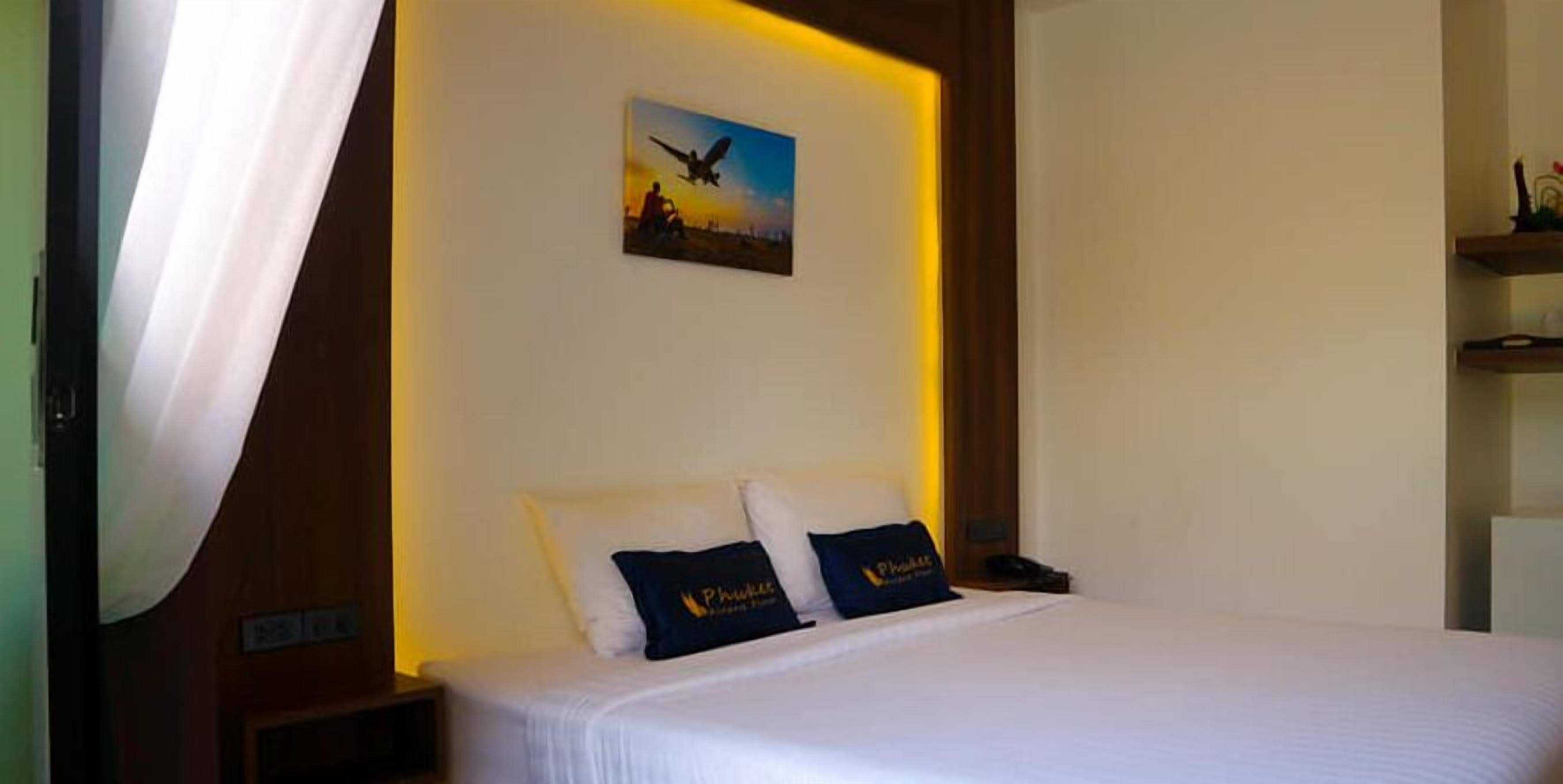 Ein Hotelzimmer mit einem Bett, zwei Kopfkissen mit einem Logo, einem Nachttisch, einem Wandbild und einem hölzernen Kopfteil.