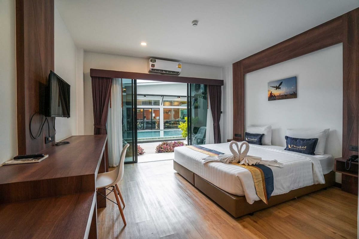 A modern hotel room with a large bed, a desk, and a view of a pool and building through glass doors.