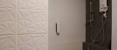 A bathroom with a white textured wall, a towel dispenser, and a shower with a handheld showerhead and hose.