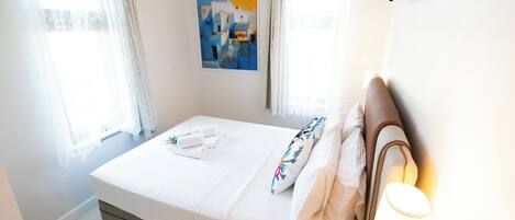 Una habitación de hotel con una cama, un cuadro en la pared y una ventana con cortinas.