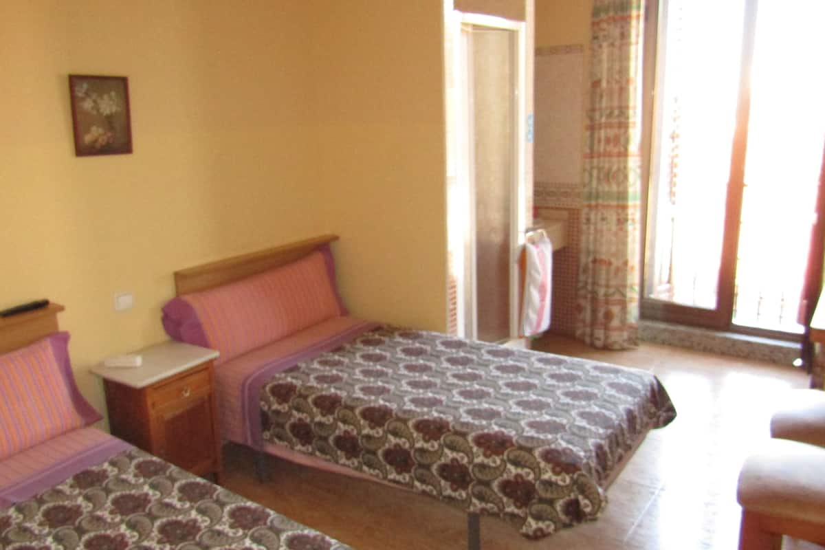 Una habitación con dos camas, una mesita de noche, una silla y una ventana con cortinas.