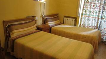 Une chambre avec deux lits simples, une table de chevet, une lampe et une fenêtre avec des rideaux.