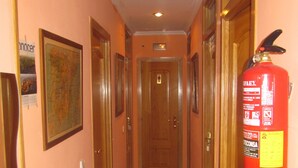 A hallway with wooden doors, a fire extinguisher mounted on the wall, and a radiator on the floor. - Pensión Mollo (Madrid)