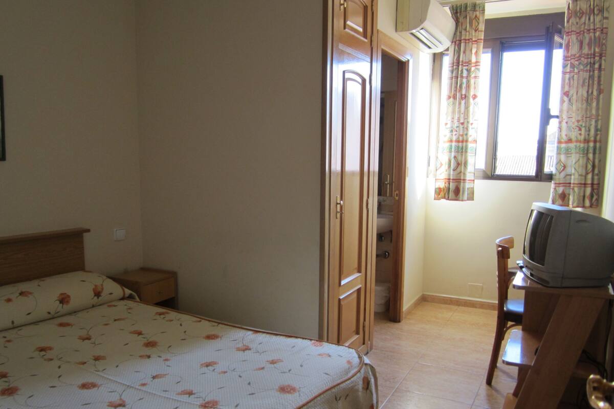 Un dormitorio con una cama, un escritorio con televisor y una ventana con cortinas.