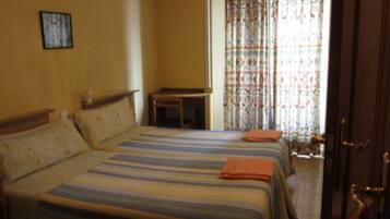 A hotel room with two beds, a small table, and a window with curtains.