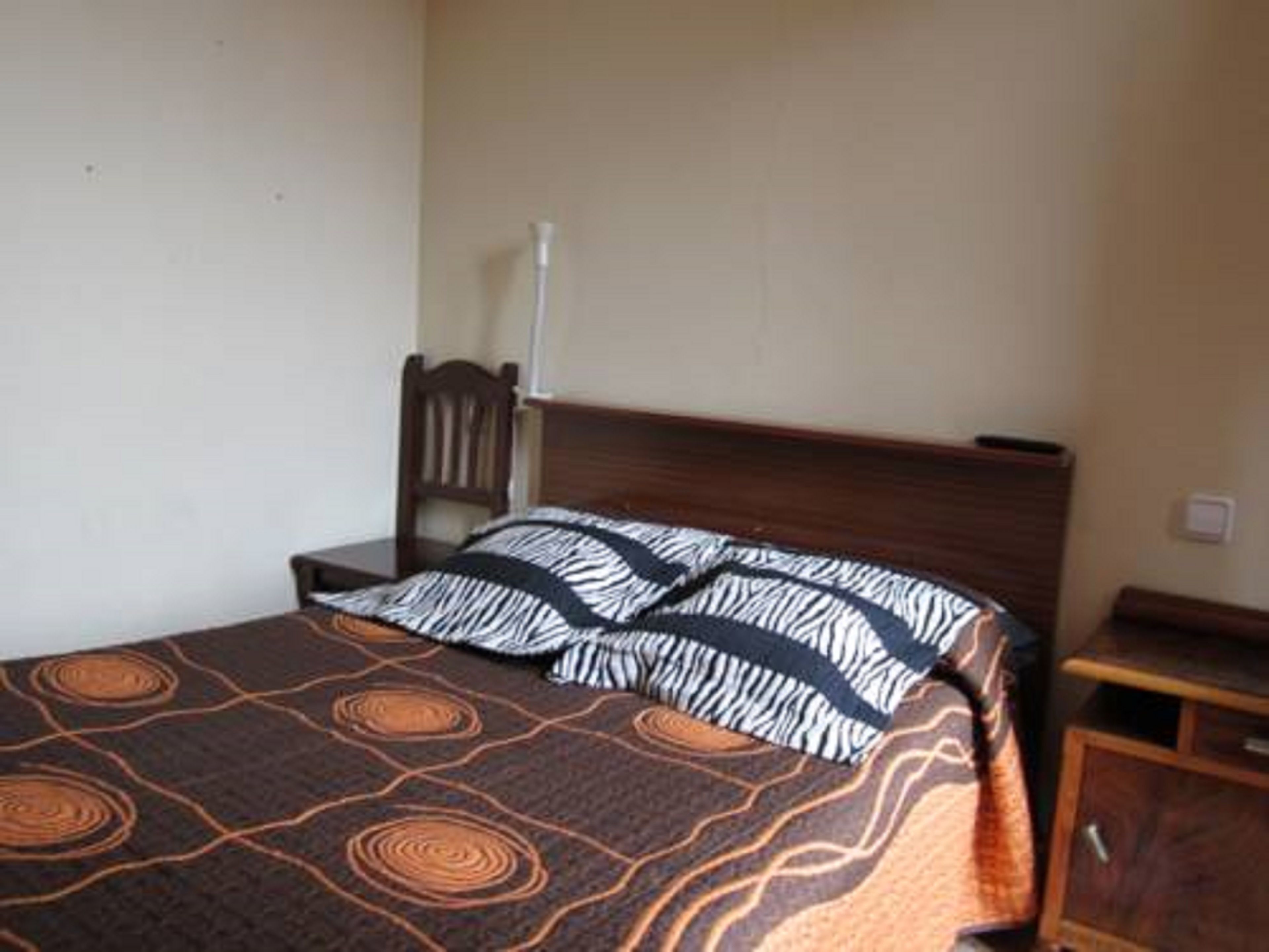 A single bed with a zebra-patterned blanket, a wooden headboard, a nightstand, and a wooden cabinet.