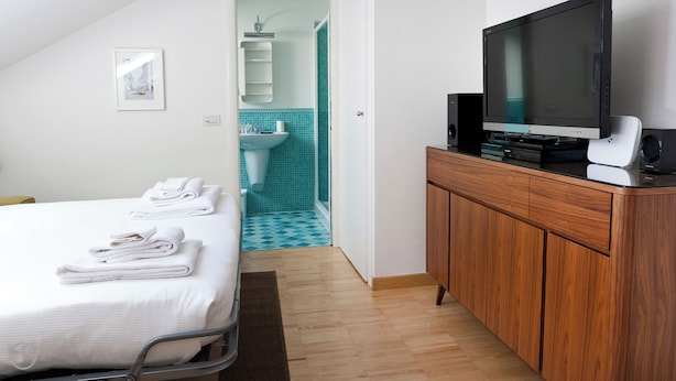 A hotel room with a bed, a TV, a wooden cabinet, and a bathroom with blue tiles. - Italianway   - Alessi (Milan)