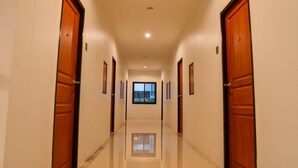 A hotel hallway with wooden doors, a reflective floor, and a window at the end. - S2 Airport Residence (Sa Khu)