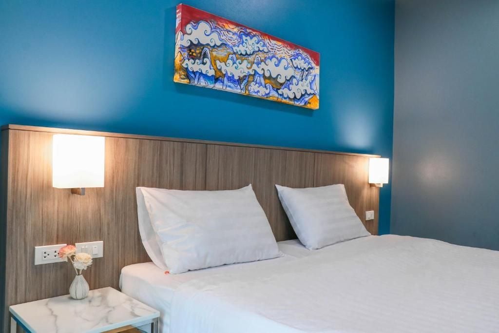 Ein Hotelzimmer mit einem Bett, Nachttischlampen, einem Nachttisch mit Blumenvase und einem farbenfrohen Gemälde an der Wand.