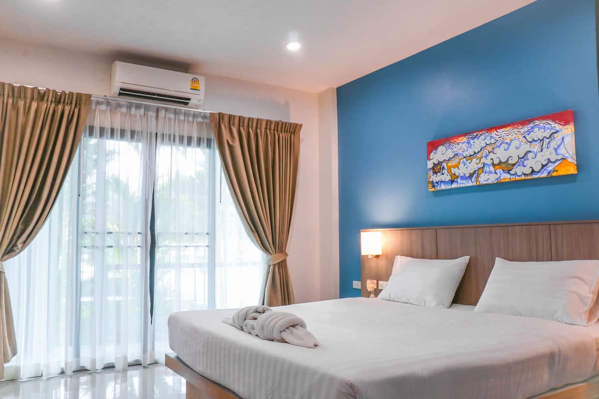 A hotel room with a large bed, a painting on the wall, and an air conditioning unit.