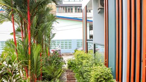 A modern building with a narrow pathway flanked by lush greenery and a palm tree. - S2 Airport Residence (Sa Khu)