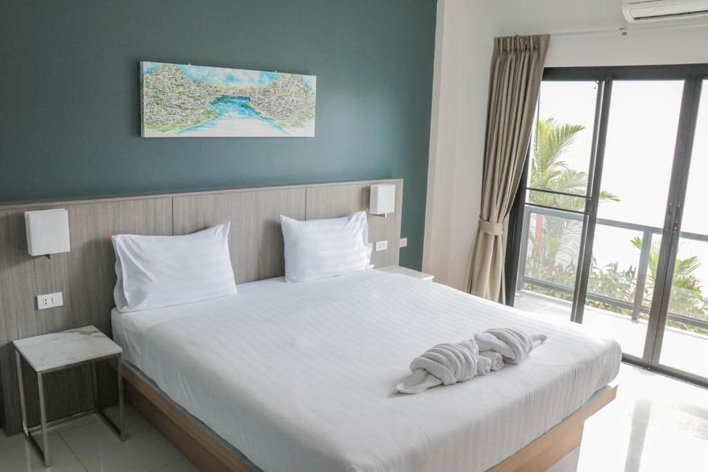 Quarto de hotel com cama grande, mesa de cabeceira, quadro na parede e vista para o exterior.