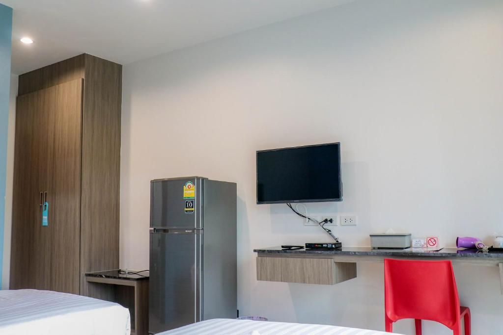 Una camera d'albergo con un letto, una scrivania con un computer, una televisione, un frigorifero e un armadio.