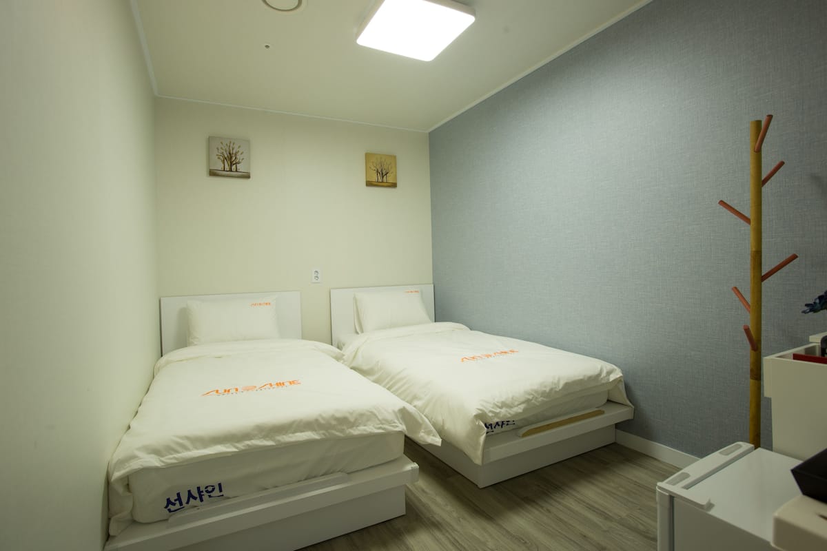 Een kleine, schone kamer met twee eenpersoonsbedden, een houten kapstok en een klein bureau met stoel.