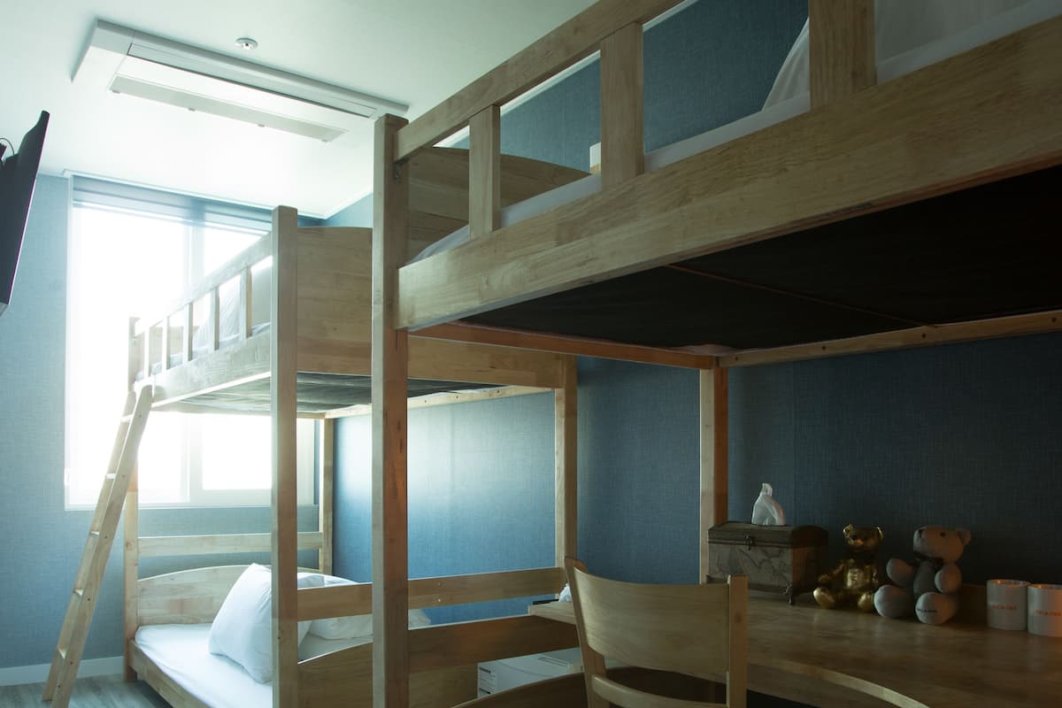 Een slaapkamer met een stapelbed, bureau en stoel, een raam en een plafondlamp.