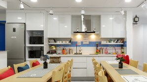 Une cuisine moderne avec des meubles blancs, un réfrigérateur en acier inoxydable, un four à micro-ondes et un coin repas comprenant des chaises et une table en bois.
