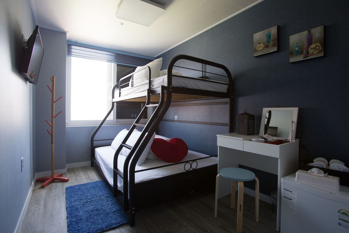 Een slaapkamer met stapelbed, bureau, stoel en een televisie aan de muur.