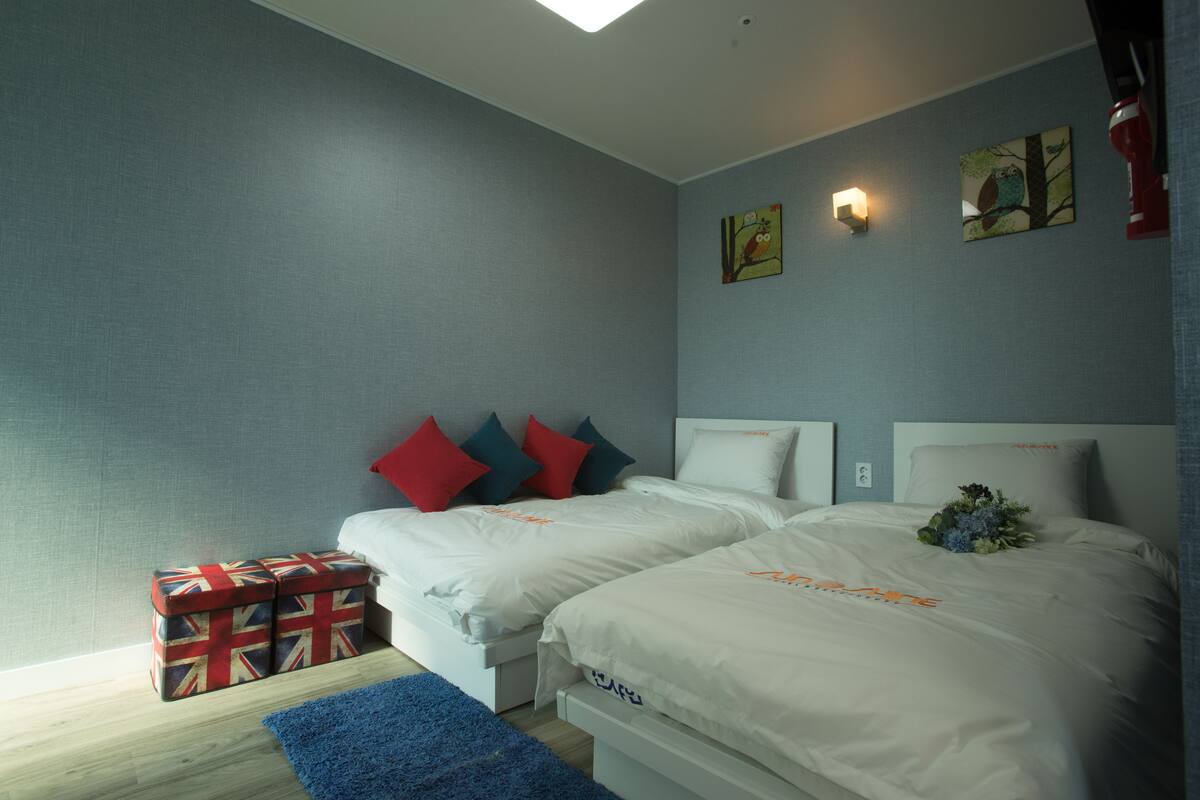 Een slaapkamer met twee bedden, een blauw vloerkleed en een cadeaudoos.