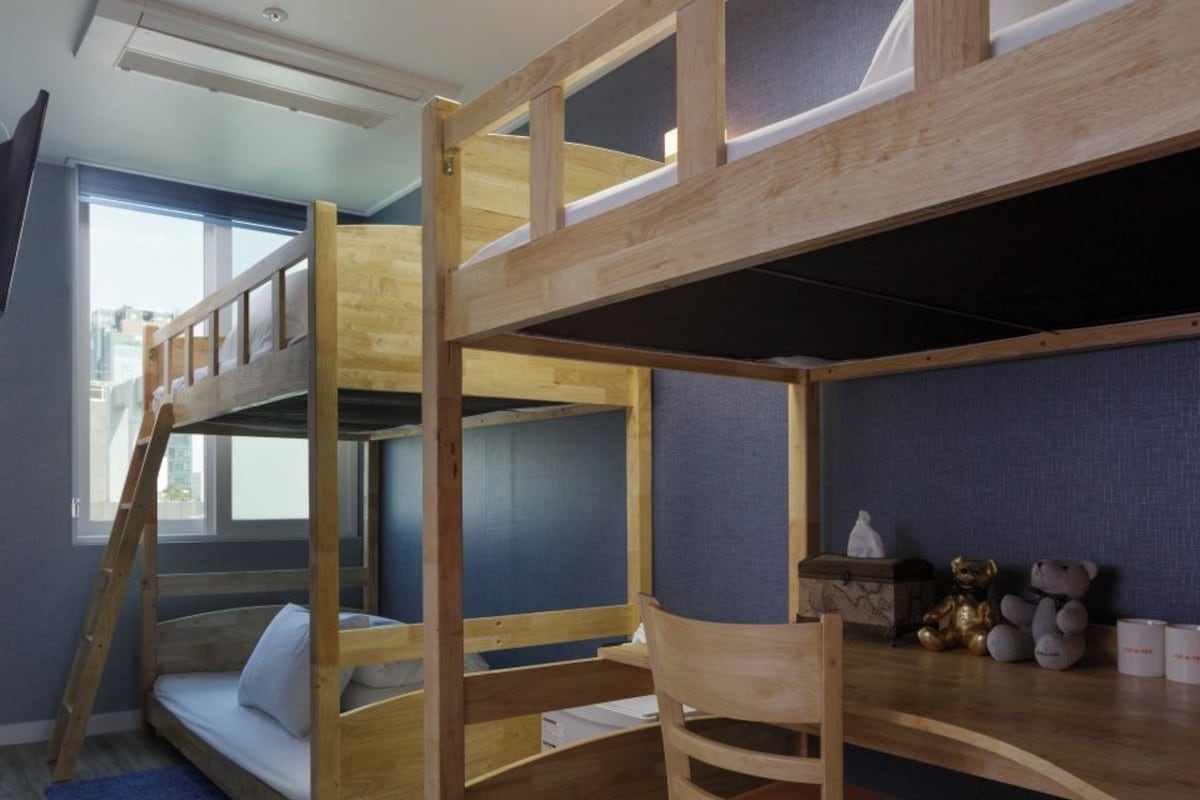 Ein Stockbett mit Schreibtisch und Stuhl, ein Fenster und eine blaue Matte auf dem Boden.