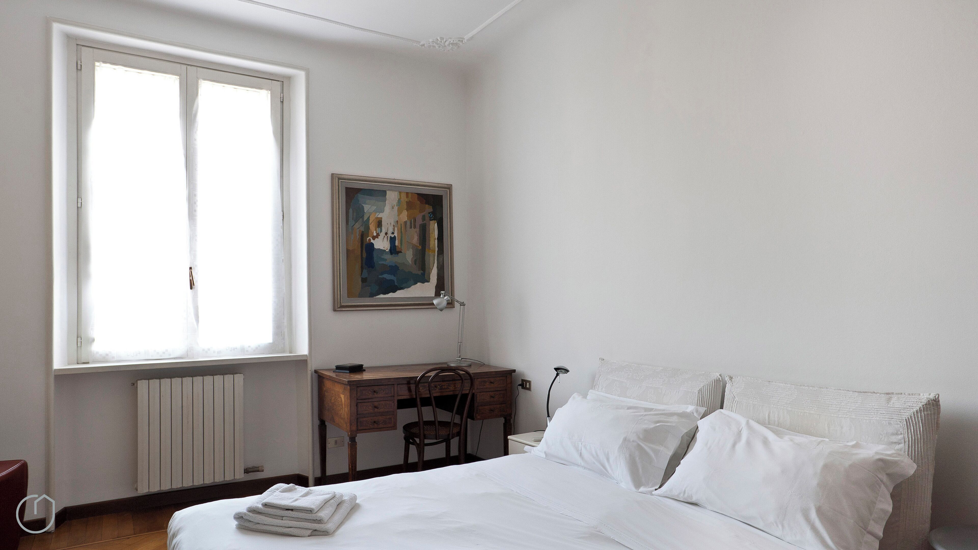 A bedroom with a bed, a desk, a chair, a radiator, and a window.