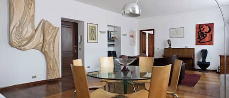 A modern dining area with a glass table and wooden chairs, a piano, and abstract art on the walls.