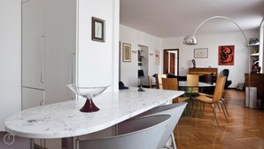 Una cucina moderna con un piano di lavoro in marmo, un'area pranzo con sedie in legno e un corridoio che dà sull'area soggiorno.