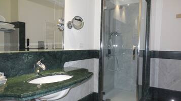 Un baño moderno con lavamanos de mármol, cabina de ducha con paredes de vidrio y un espejo.