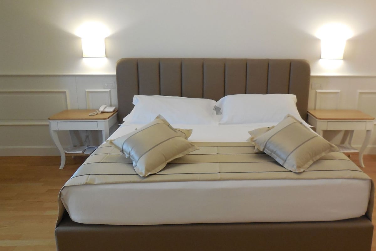 Uma cama bem arrumada com um edredom listrado, dois travesseiros e duas mesas de cabeceira com abajures.