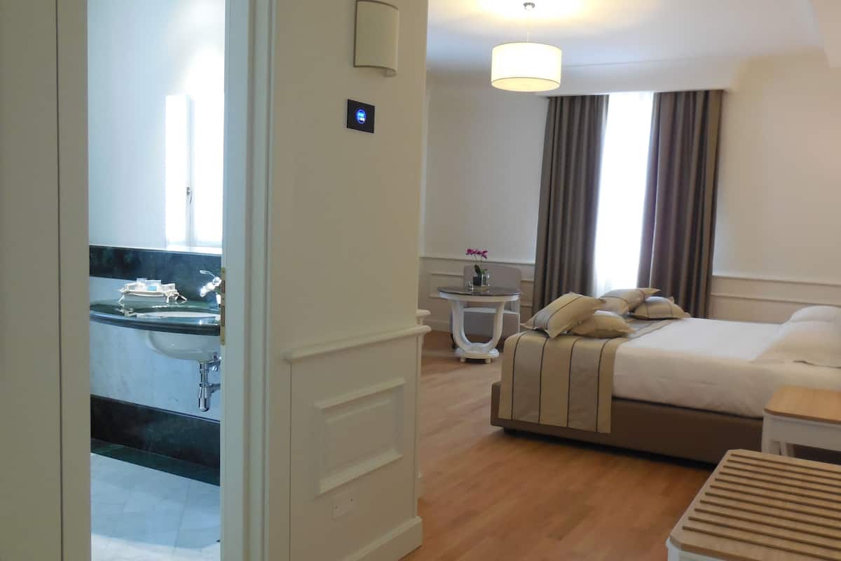 A hotel room with a bed, bedside table, lamp, and a small table with a vase of flowers.