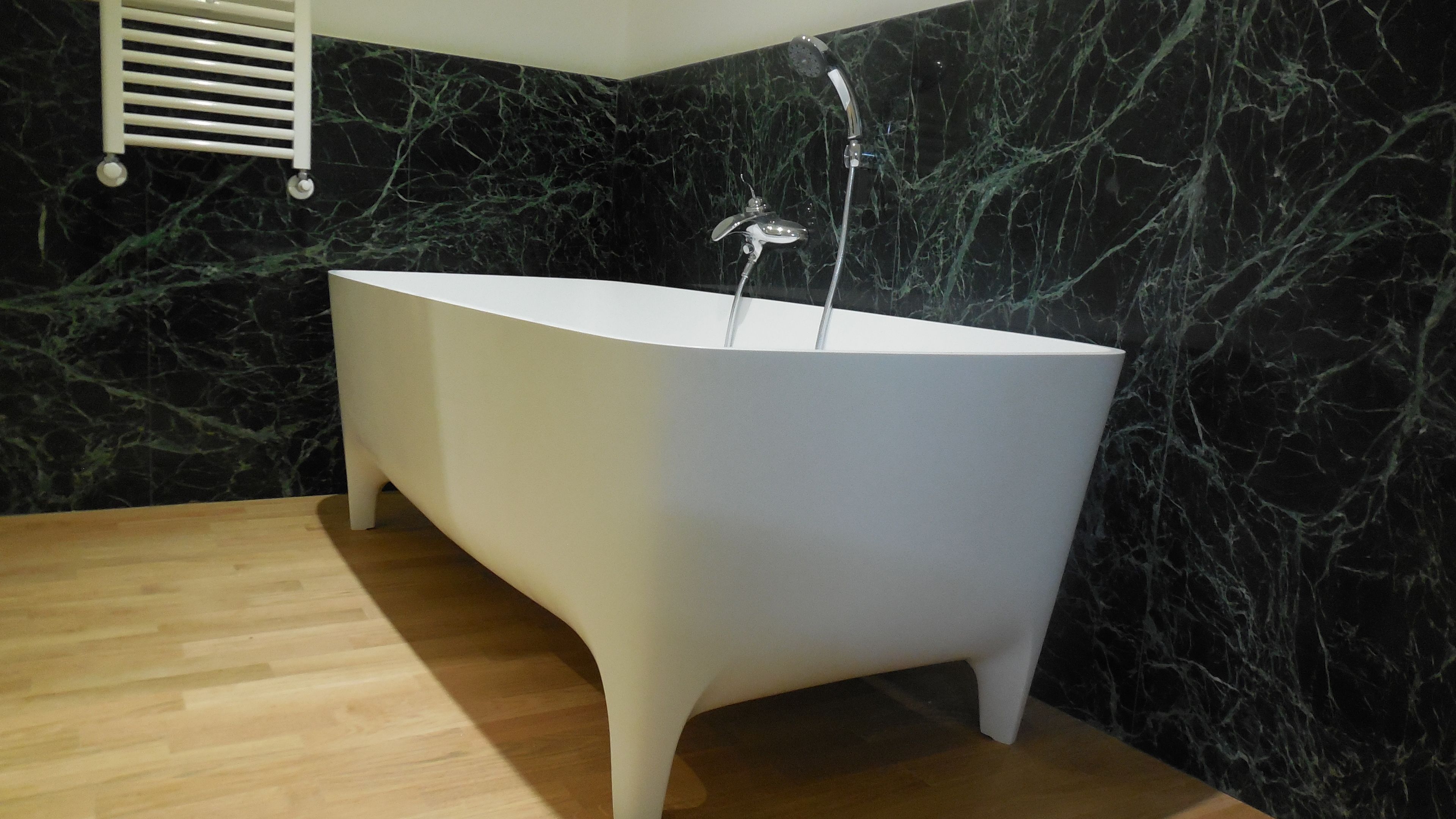 A modern bathroom with a freestanding bathtub, marble walls, and a wooden floor.
