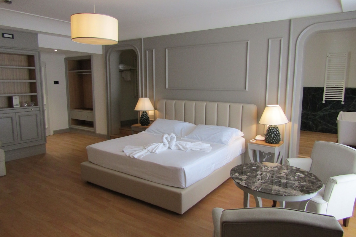 Habitación de hotel con una cama grande, dos mesitas de noche con lámparas, una mesa redonda, una silla y un armario.