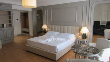 A hotel room with a large bed, two bedside tables with lamps, a round table, a chair, and a wardrobe.