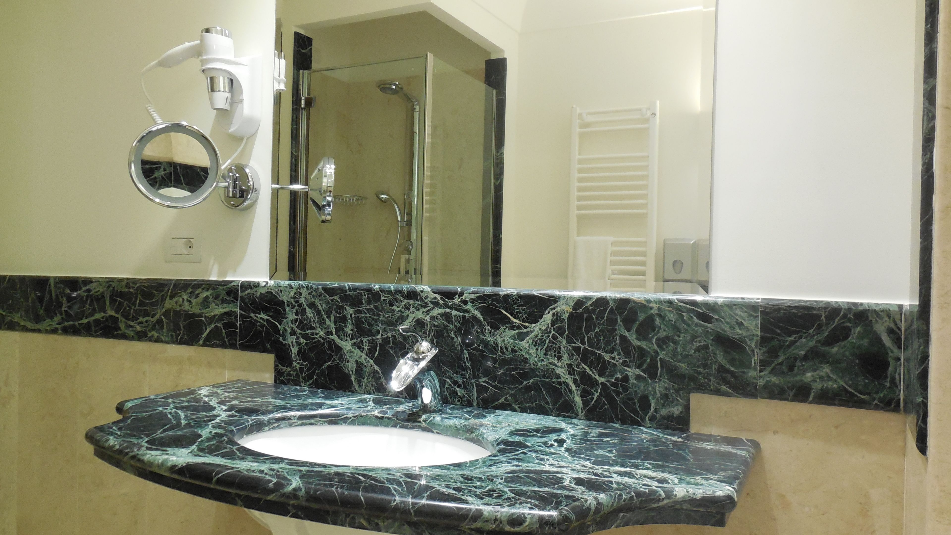 Un baño con lavamanos de mármol, un espejo y una cabina de ducha con paredes de vidrio.