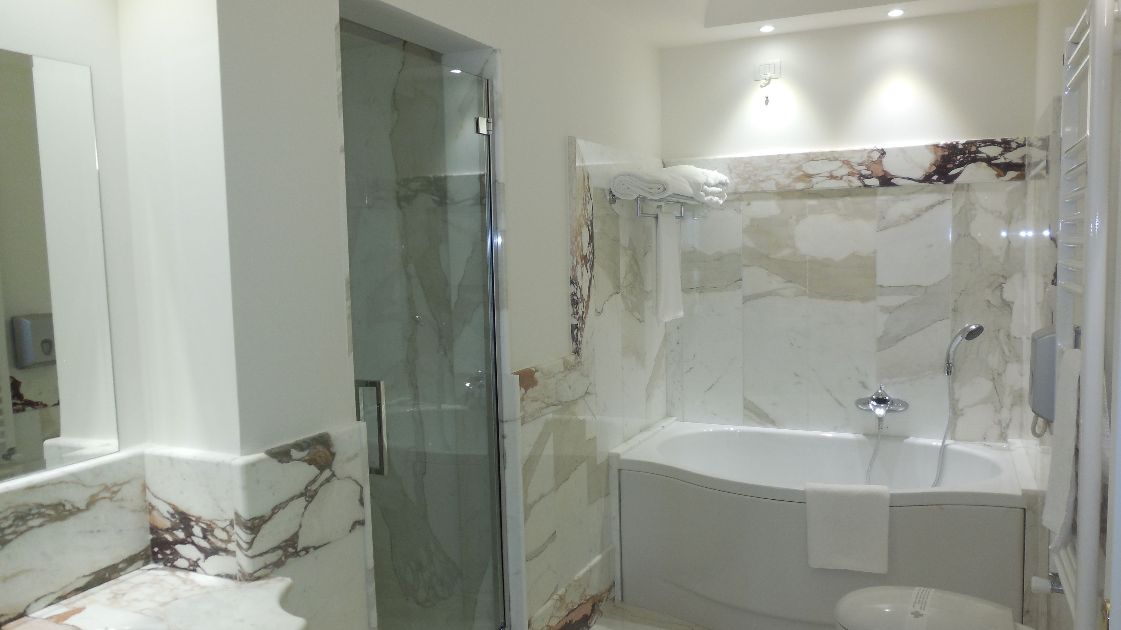 Un baño moderno con ducha envuelta en vidrio, una bañera y paredes de mármol.
