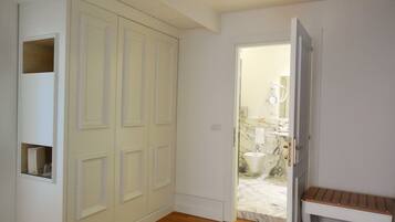 Un pasillo con una puerta cerrada, un banco y un baño visible a través de una puerta abierta.