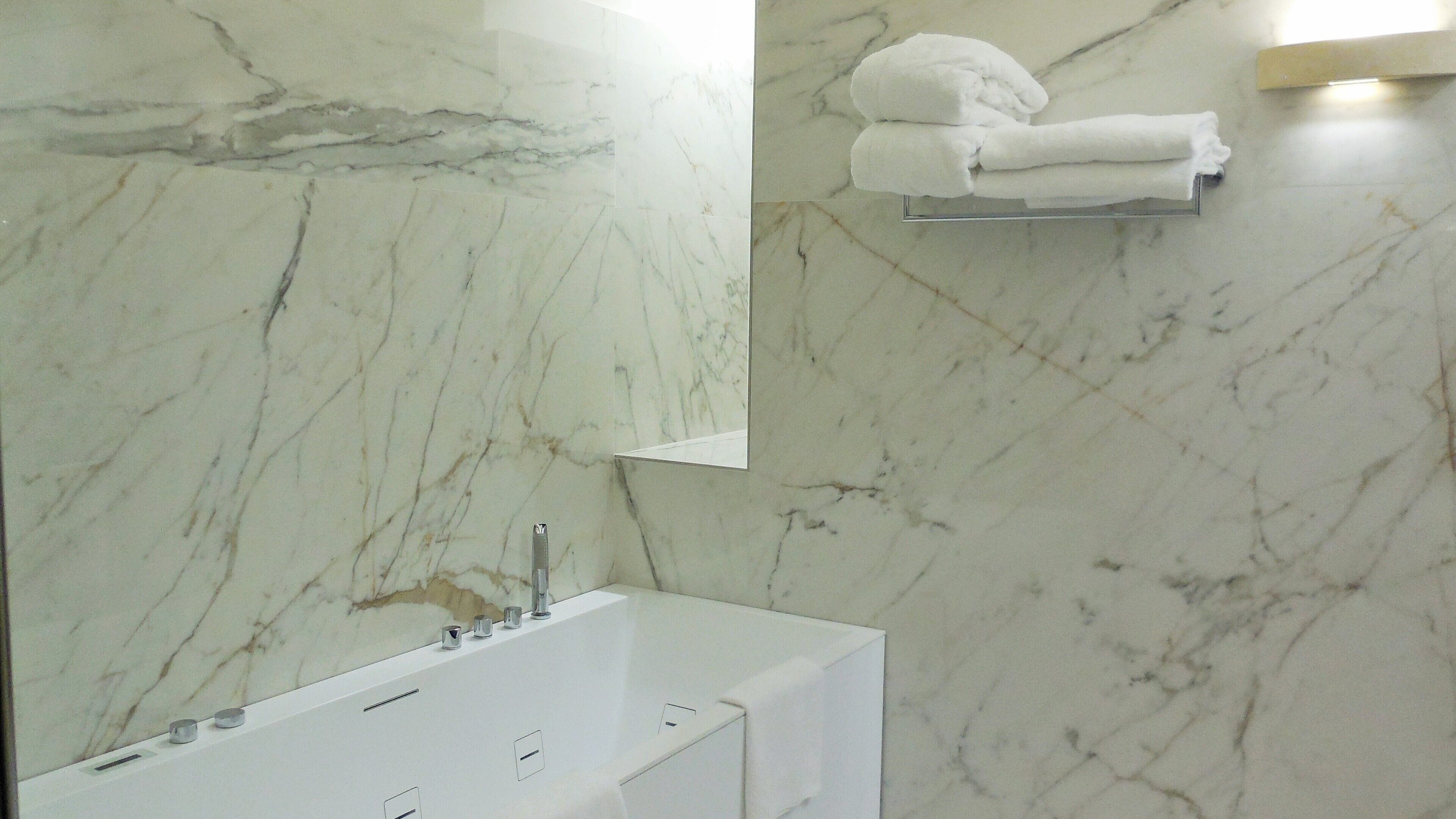 A bathroom with a marble wall, a bathtub, and a towel rack with folded towels.