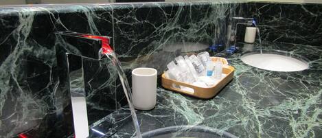 Un baño con encimera de mármol, lavamanos, espejo y secamanos.