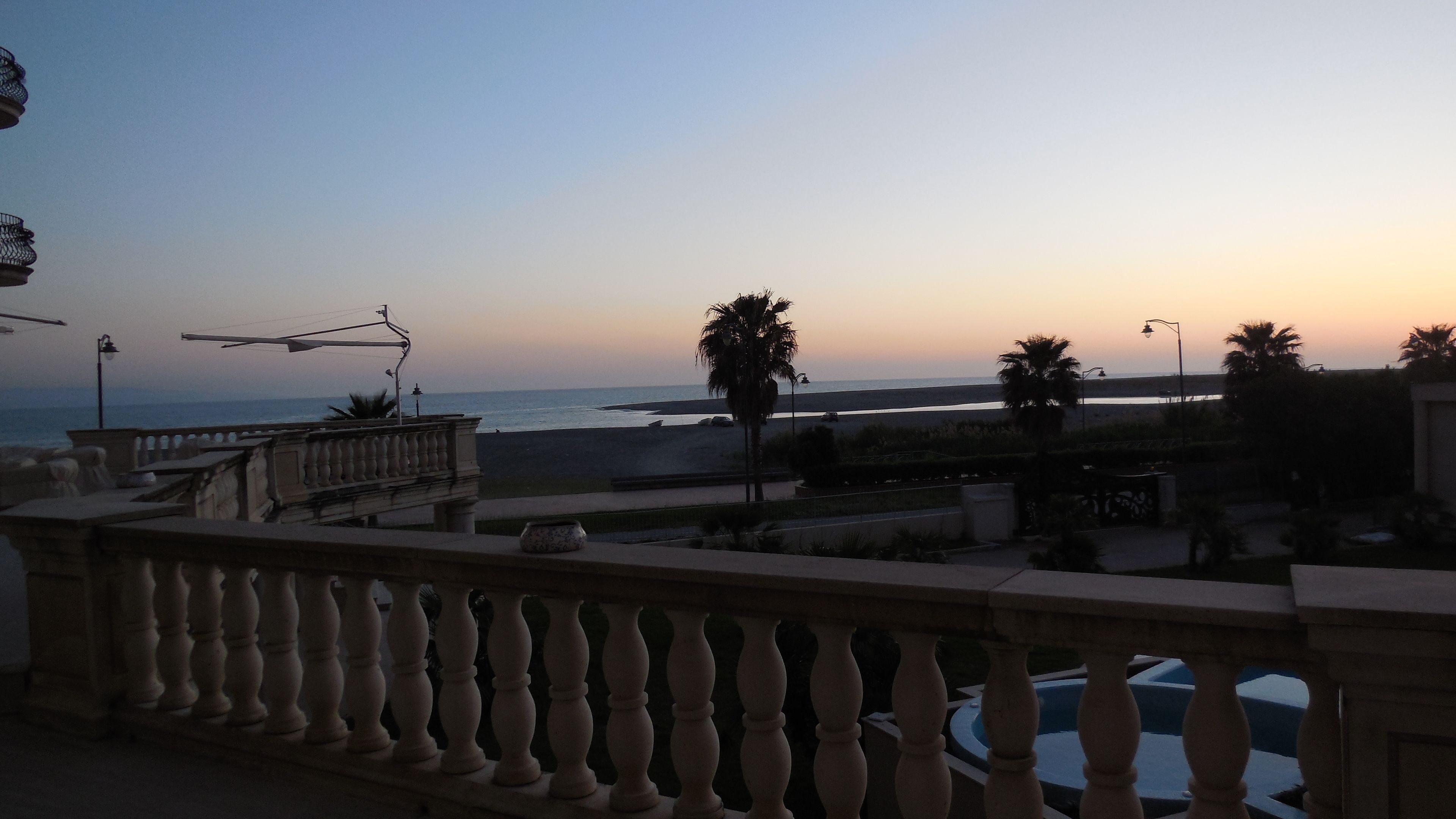 A balcony with a view of the beach and ocean during sunset.