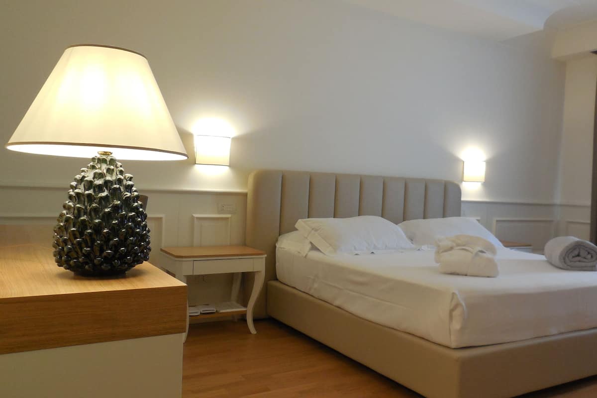 A hotel room with a bed, bedside table, lamp, and a chair.