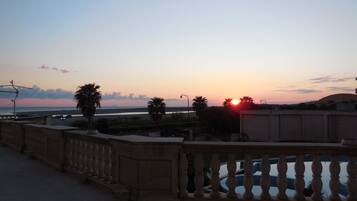 Ein Sonnenuntergangsblick von einem Balkon mit Blick auf einen Strand, Palmen und eine Straße.
