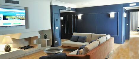 A modern living room with a sofa, armchairs, a coffee table, and a flat-screen TV mounted on the wall.