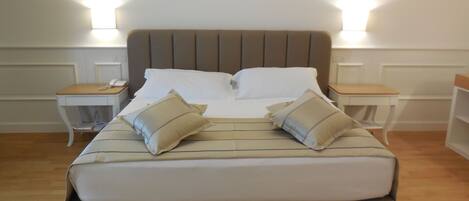 A neatly made bed with a striped bedspread and two pillows, flanked by bedside tables with lamps, in a room with wooden flooring and white walls.