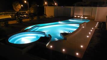 Una piscina de diseño curvo, rodeada por un muro bajo e iluminada por luces.