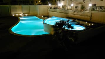 Relax by the illuminated pool, surrounded by a traditional building with a balcony and balustrade.