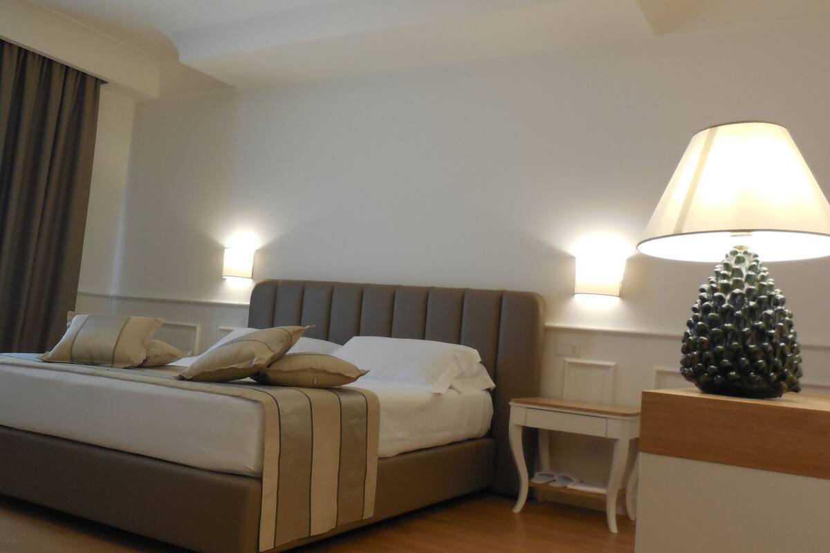 A neatly made bed with pillows, a bedside lamp, and a nightstand in a hotel room.