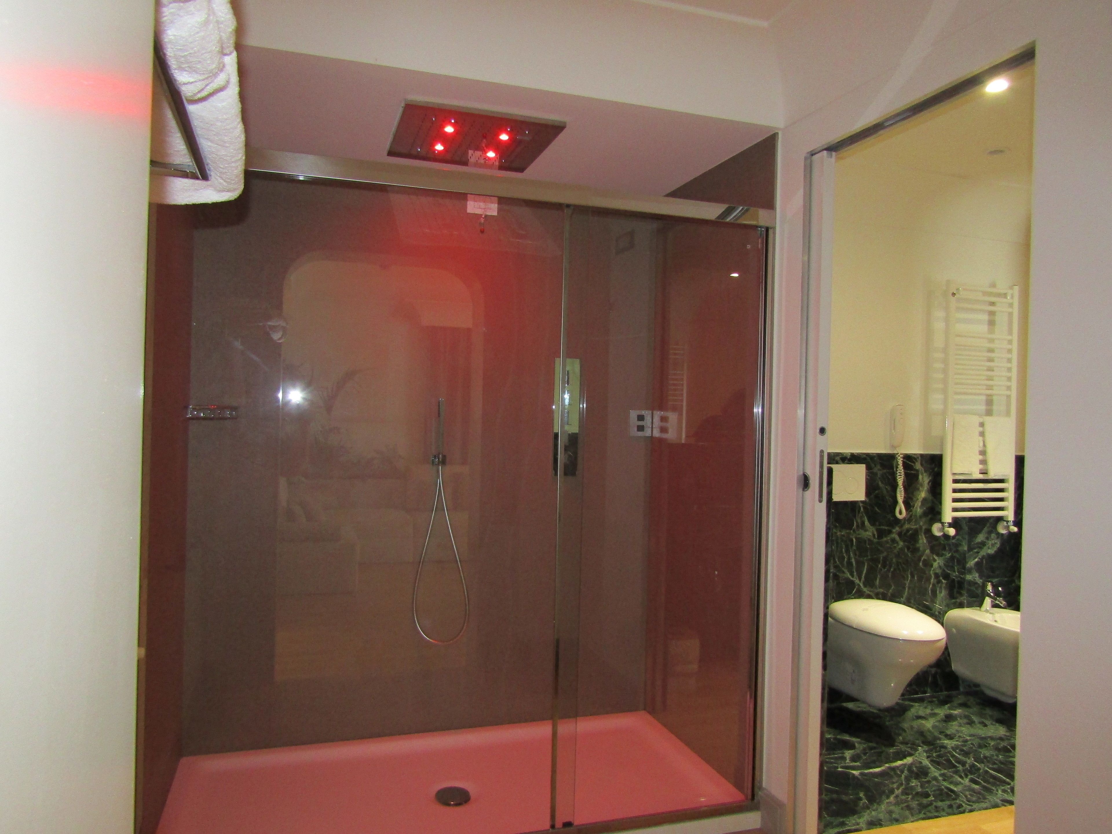 Une cabine de douche fermée par des parois en verre, dotée d’un siège rouge, d’un sèche-mains visible et d’une porte en verre.