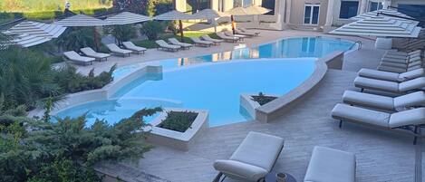 A pool area with lounge chairs, a swimming pool, and surrounding greenery.