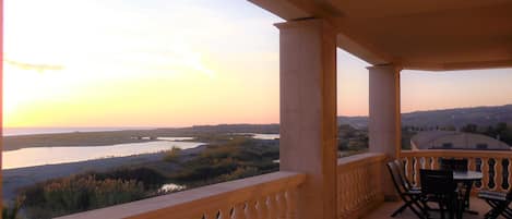 Un balcón con vista a un río y colinas lejanas, amueblado con una mesa y sillas.